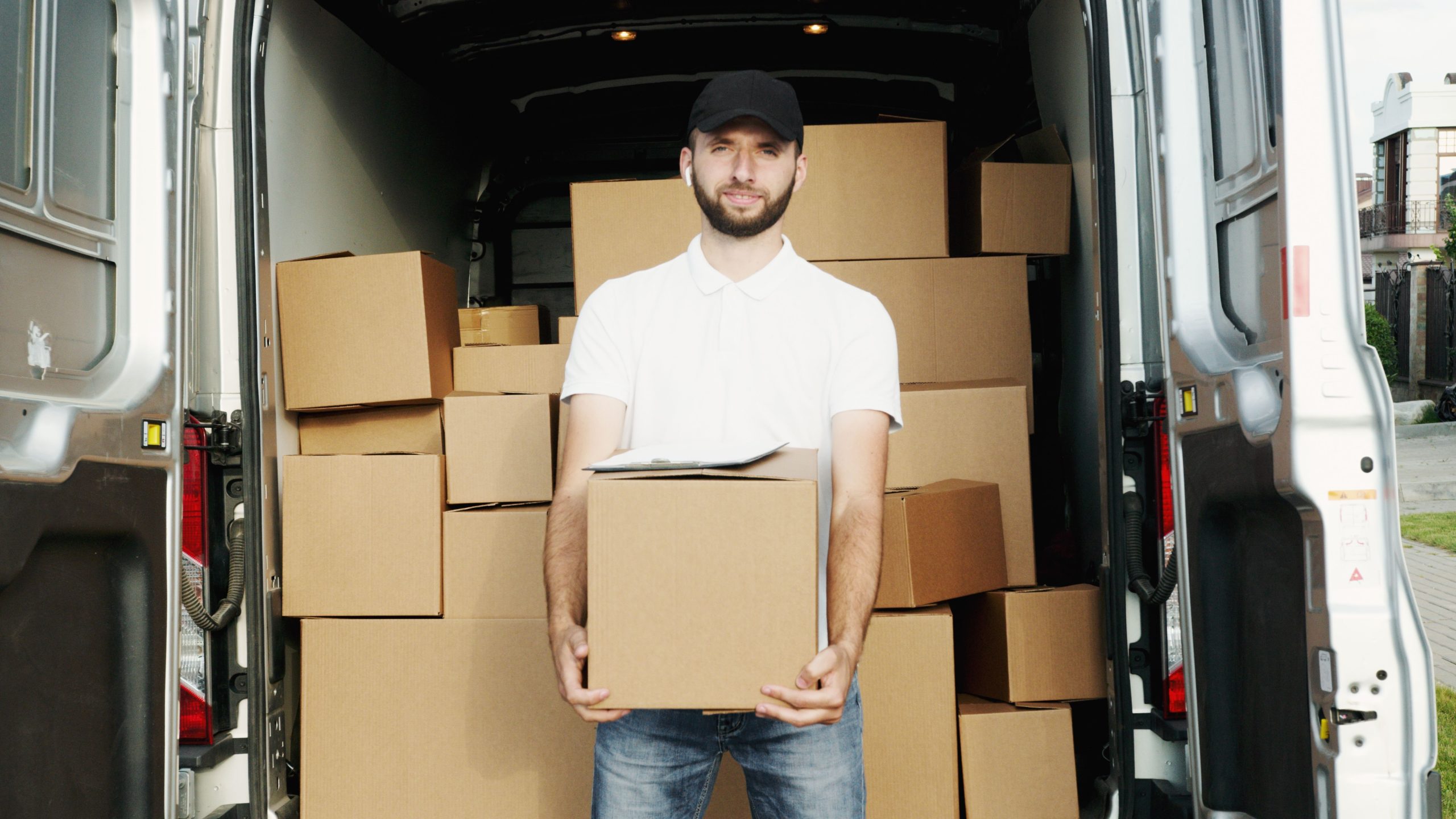 A courier standing at the back of a van holding a package for delivery.